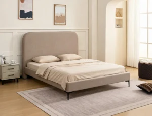 Beige upholstered bed on slim black metal legs in a panelled room, bedside table to the left